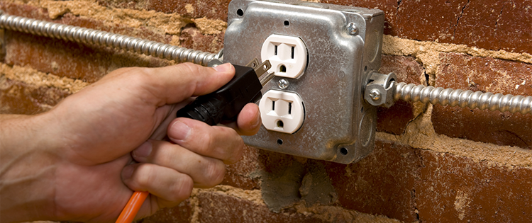 一只手将电源线插入安装在砖墙上的电源插座